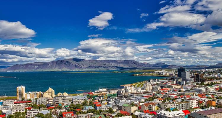 Helder panoramisch uitzicht op Reykjavik met een opvallende blauwe baai en bergachtergrond onder verspreide wolken.