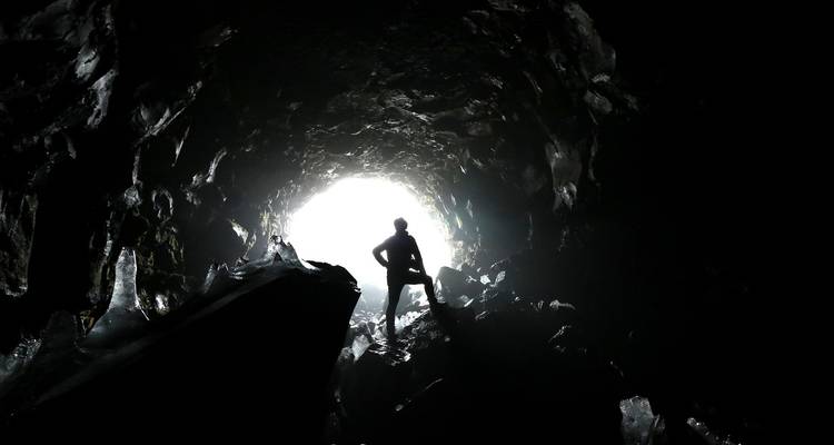 Un aventurier en silhouette se tient à l'entrée lumineuse d'une grotte de glace sombre