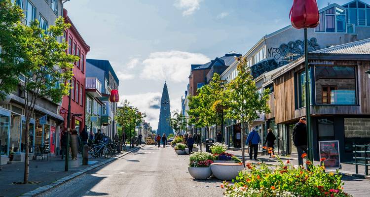 Rue principale colorée de Reykjavik bordée de commerces et de fleurs, avec la Hallgrimskirkja s'élevant à l'horizon
