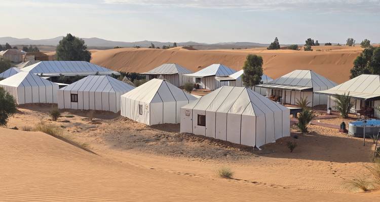 Grupo de tiendas de lona blanca dispuestas entre las dunas bajas del Sahara en un campamento del desierto.