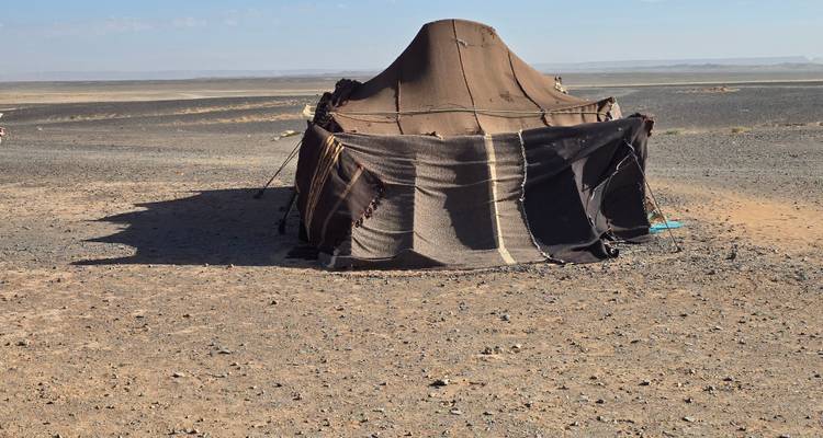 Tienda de campaña de nómada solitario hecha de tela tejida oscura parada en una llanura desértica rocosa.