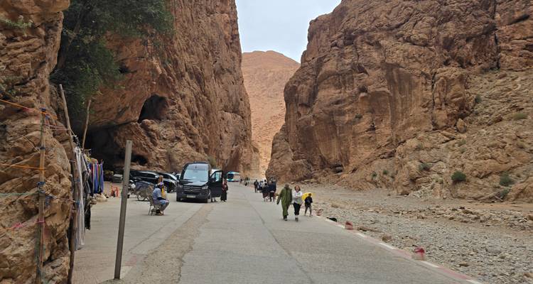 Los visitantes caminan y compran en el estrecho camino del cañón de la Garganta de Todra, flanqueado por acantilados rojos imponentes.
