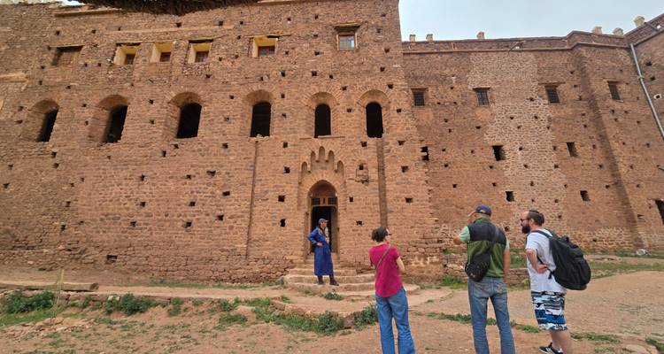 Guía hablando con visitantes fuera de una antigua kasbah de adobe con muchas ventanas