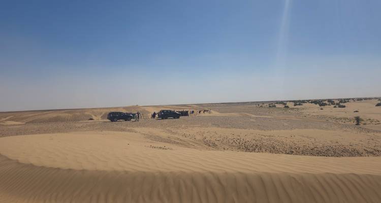 Vasta vista desértica con vehículos todoterreno y dunas ondulantes y suaves bajo un cielo azul
