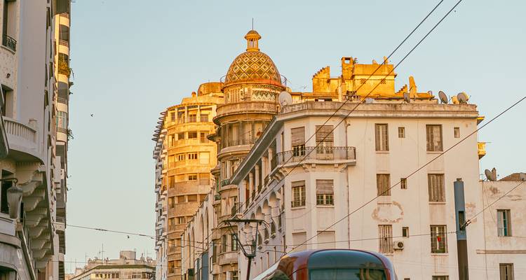 Edificios históricos art-déco del centro de Casablanca brillando bajo la cálida luz del atardecer con cables de tranvía arriba.