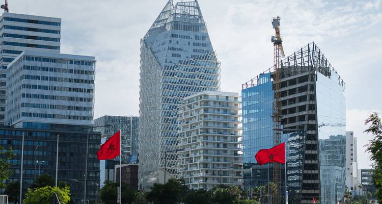 Rascacielos modernos de cristal y grúas de construcción en el distrito comercial de Marruecos con banderas nacionales ondeando.