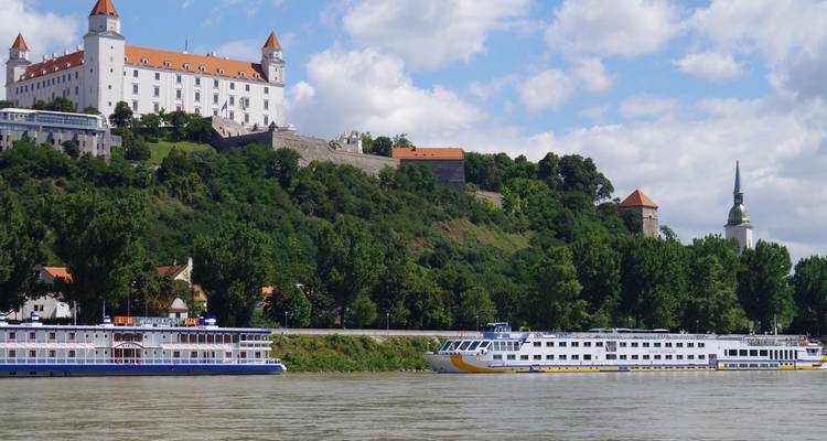 Le Château de Bratislava surplombant le Danube avec des navires de passagers et la flèche de la Cathédrale Saint-Martin.