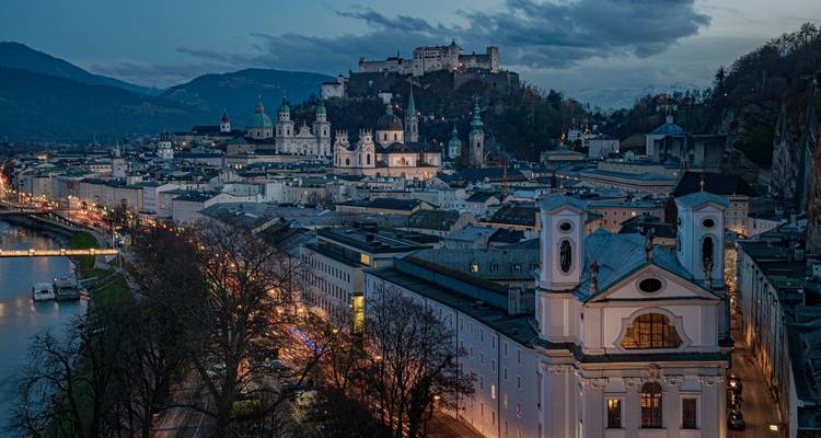 Panorama en soirée de la vieille ville de Salzbourg avec la forteresse de Hohensalzburg illuminée dominant la ligne d'horizon baroque.