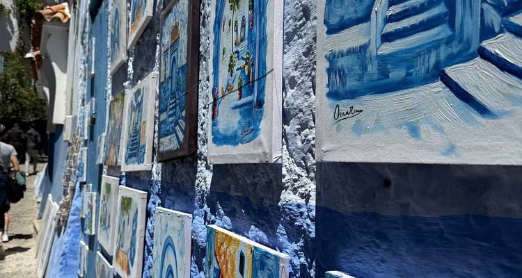 Primer plano de lienzos de arte pintados de azul expuestos a lo largo de un callejón soleado en Chefchaouen
