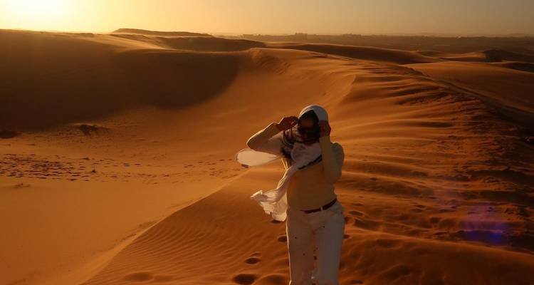 Mujer sosteniéndose contra el viento en las dunas doradas del Sahara al atardecer