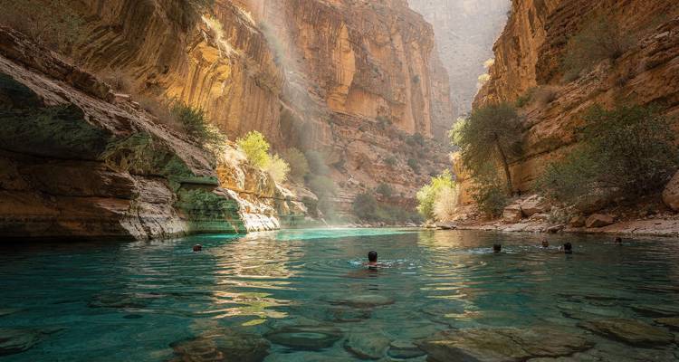 Zwemmers die genieten van smaragdgroen water in een dramatische zandsteencanyon verlicht door zonnestralen