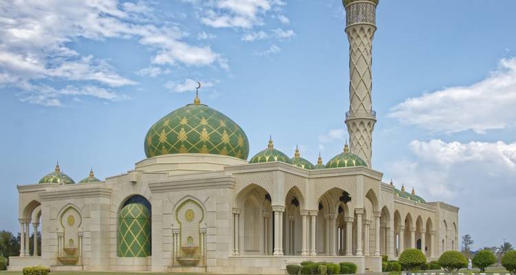 Elegante witte moskee met groene koepels en slanke minaret onder blauwe hemel