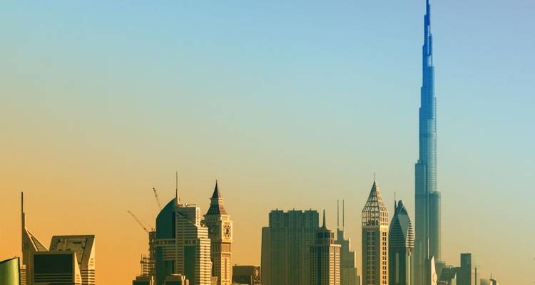 Skyline moderne de Dubaï dominée par la Burj Khalifa sous un ciel à l'aube aux teintes pastel.