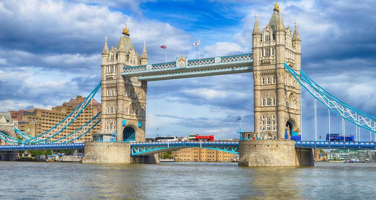 Die ikonische Tower Bridge über der Themse unter dramatischem Himmel, ein Doppeldeckerbus überquert sie.