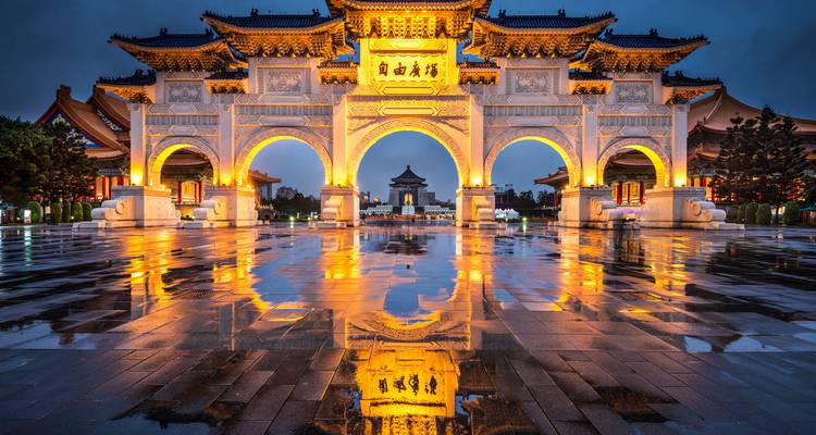 Beleuchtete Tore des Liberty Square in Taipei, die sich in einem regennassen Platz bei Einbruch der Dämmerung spiegeln.