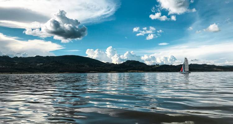Des eaux calmes du lac reflétant un ciel dramatique avec un voilier solitaire glissant sur la surface.