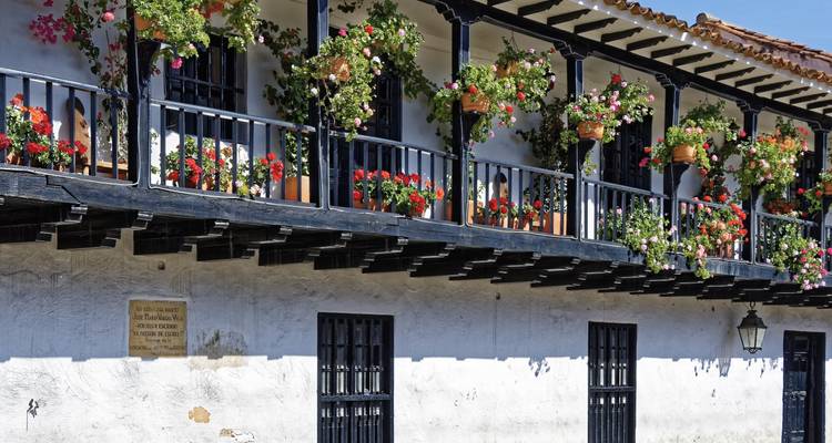Balcon colonial traditionnel débordant de pots de fleurs colorés contre un mur blanchi à la chaux.