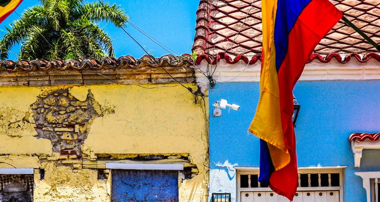 Le drapeau colombien éclatant flotte au-dessus des façades coloniales colorées sous un ciel bleu éclatant.