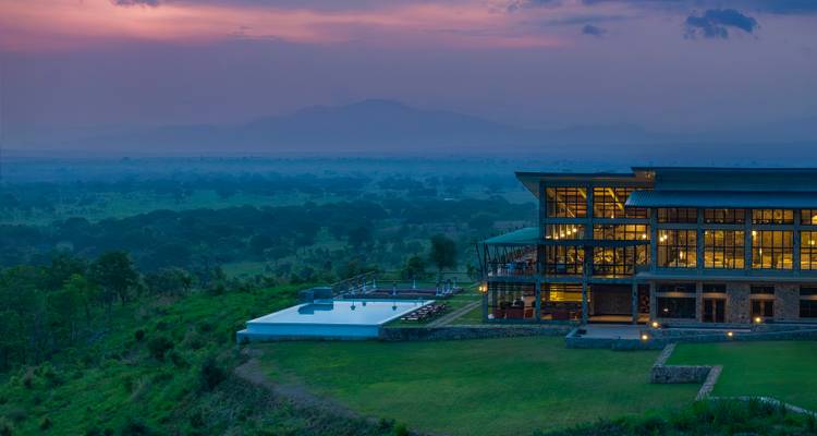 Dusk aerial view of a hilltop lodge, infinity pool and vast savannah stretching into misty mountains.