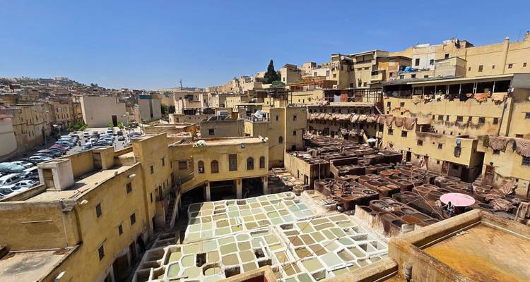 Wide view of Fes’ Chouara Tannery with rows of colorful leather-dyeing vats surrounded by yellow medieval buildings under a clear blue sky.
