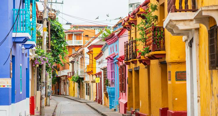 Narrow colonial street lined with vividly painted houses, balconies, and flowering vines.