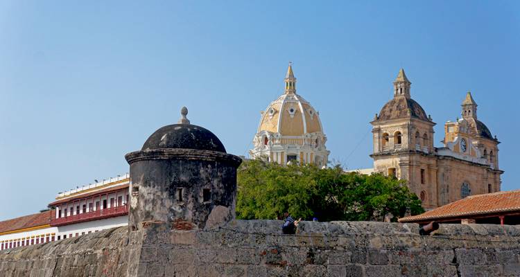 Historic city wall and guard tower with the domes of Cartagena Cathedral rising against a clear sky.