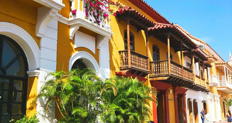 Row of restored colonial houses with balconies, plants and bright yellow façade against clear blue sky.