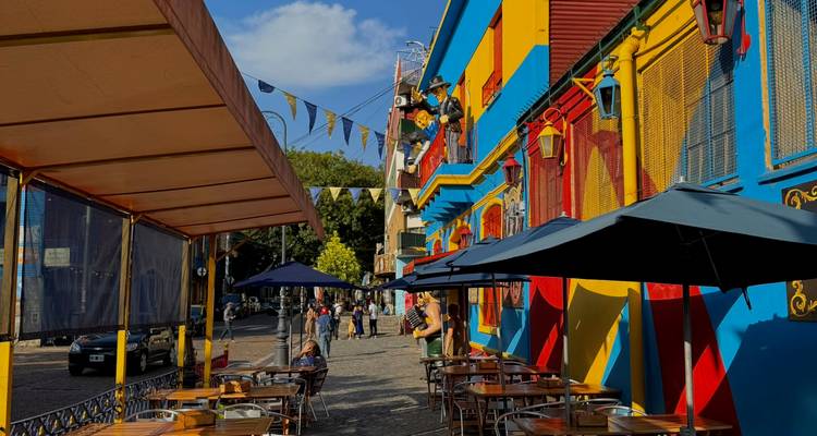 Lebendige Straße in La Boca mit leuchtend farbigen Gebäuden in Primärfarben, Außenbereichstischen von Cafés und Besuchern, die unter Wimpelketten spazieren