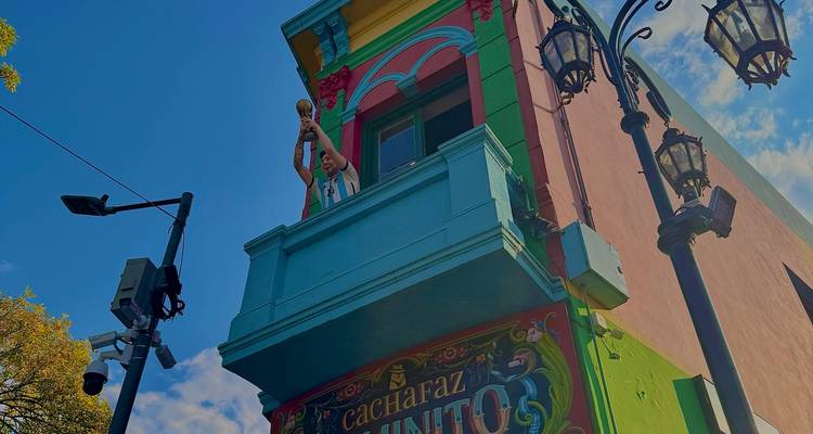 Farbenfrohe Eckengebäude in La Boca mit Statue eines Fußballfans, der einen Pokal auf einem Balkon vor blauem Himmel haelt