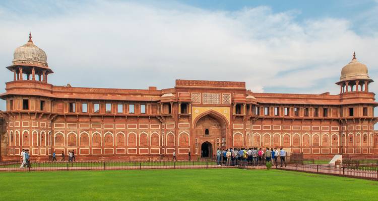 Weitläufige Ansicht der prächtigen roten Sandsteinfassade und des Tores des Agra-Forts mit Touristen auf dem grünen Rasen davor.