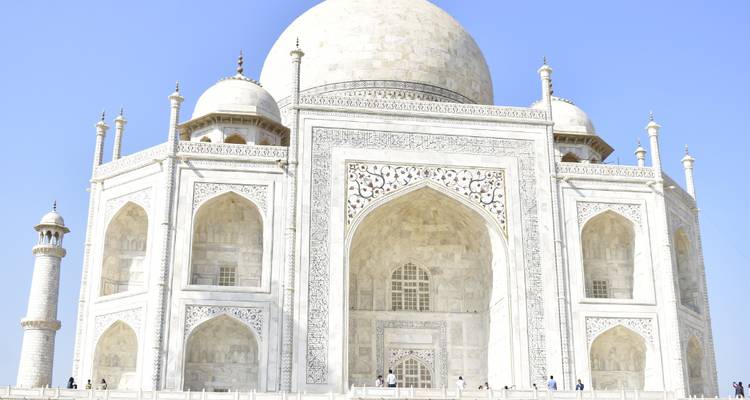 Helle Frontalaufnahme aus der Nähe des weißen Marmormausoleums des Taj Mahal vor klarem blauen Himmel.