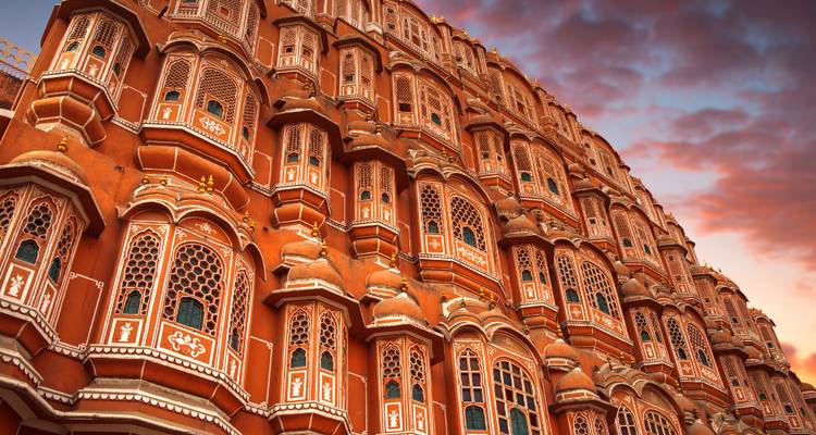 Dramatische Aufwärtsansicht der Terrakotta-Fassade des Hawa Mahal in Jaipur, das unter einem farbenfrohen Himmel bei Sonnenuntergang leuchtet.