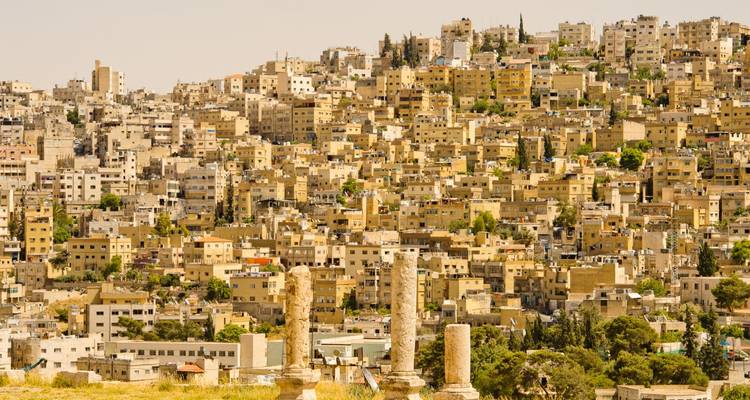 Hügeliger Sprawl aus beigen Gebäuden in Amman mit verwitterten römischen Säulen im Vordergrund