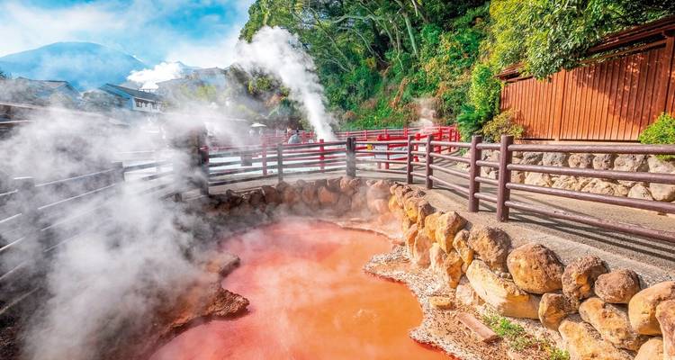 Wallende Dämpfe steigen aus leuchtend roten Thermalquellen-Becken auf, die von Holzzäunen umgeben sind, in Beppu.