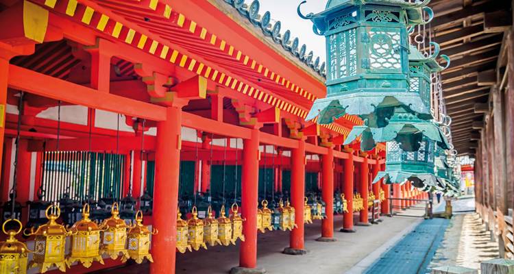 In den leuchtend roten Korridoren des Kasuga Taisha-Schreins hängen verzierte grün-goldene Laternen in Reihen.