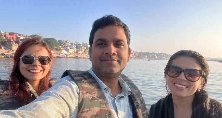 Selfie van drie vrienden in reddingsvesten op een boot met Varanasi ghats en tempels langs de oever achter hen.