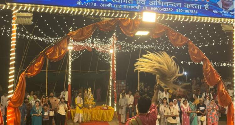 Nachtelijke Ganga Aarti-ceremonie met een priester die wierook zwaait voor een menigte onder glinsterende slingerverlichting.