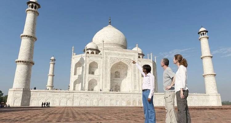 Drie reizigers bewonderen en wijzen naar het prachtige witte marmeren Taj Mahal onder een strakblauwe hemel.