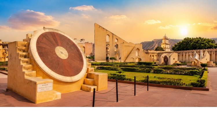 Reloj de sol antiguo y otros instrumentos astronómicos en Jantar Mantar brillando bajo el cielo dorado del atardecer.