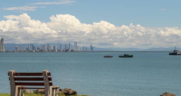 Un banco con vistas al horizonte de la Ciudad de Panamá al otro lado de una bahía azul y tranquila en un día despejado.