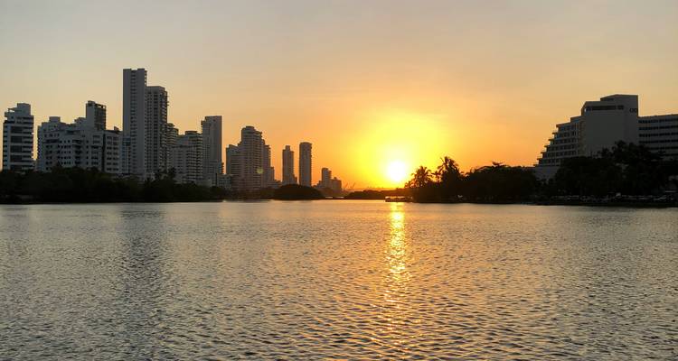 City skyline silhouettes against a golden Caribbean sunset reflected on calm bay waters.