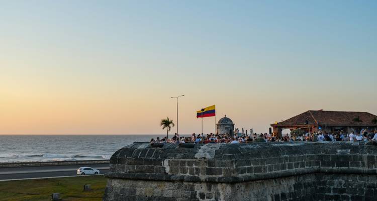 Crowds gather on Cartagena’s historic stone ramparts with a Colombian flag at dusk overlooking the Caribbean Sea.