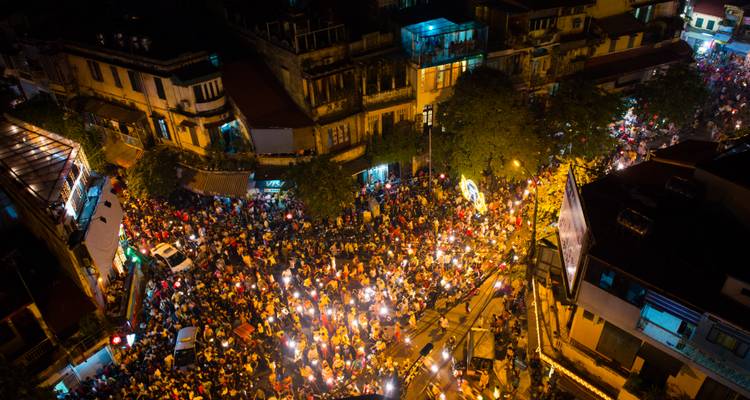Nächtliche Luftaufnahme des Hanoi Old Quarter voller Motorräder und Fußgänger unter hellen Straßenlaternen.