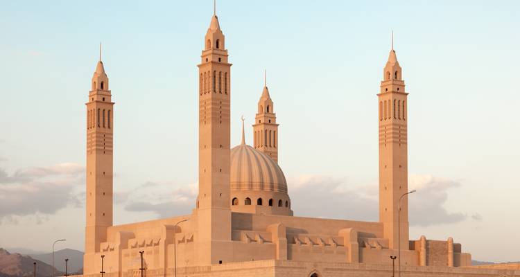 Modern mosque with central dome and four slender minarets bathed in warm evening light.