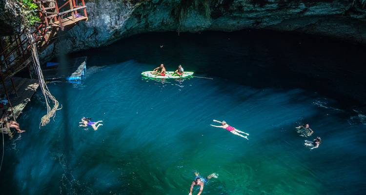Zwemmers en een kajak genieten van het diepblauwe water van een open cenote.