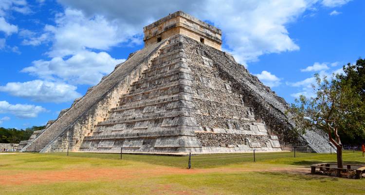La pyramide emblématique d'El Castillo à Chichen Itza s'élevant contre un ciel bleu éclatant avec des nuages épars.
