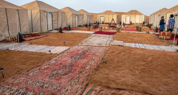Großzügiges Wüstencamp mit Reihen von beigen Zelten auf gehartem Sand und gemusterten Teppichen.