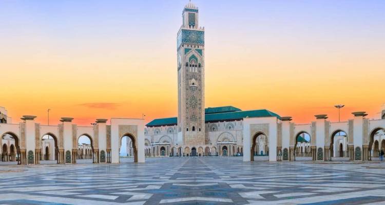 Mosquée Hassan II et haut minaret encadrés par des arcades au lever du soleil avec un ciel aux tons pastel à Casablanca