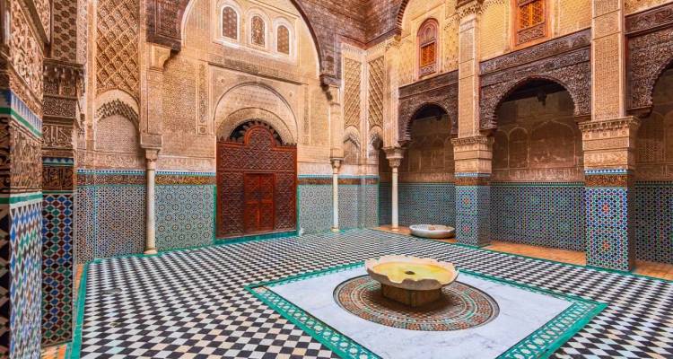 Cour ornementée d'une madrasa historique présentant des carreaux de mosaïque complexes, des arcs sculptés et une fontaine centrale