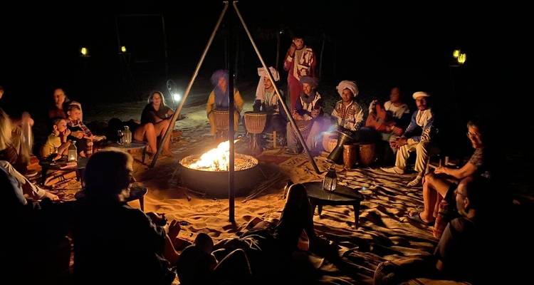 Les voyageurs se rassemblent autour d'un feu de camp avec des tambours sous la nuit désertique sans étoiles